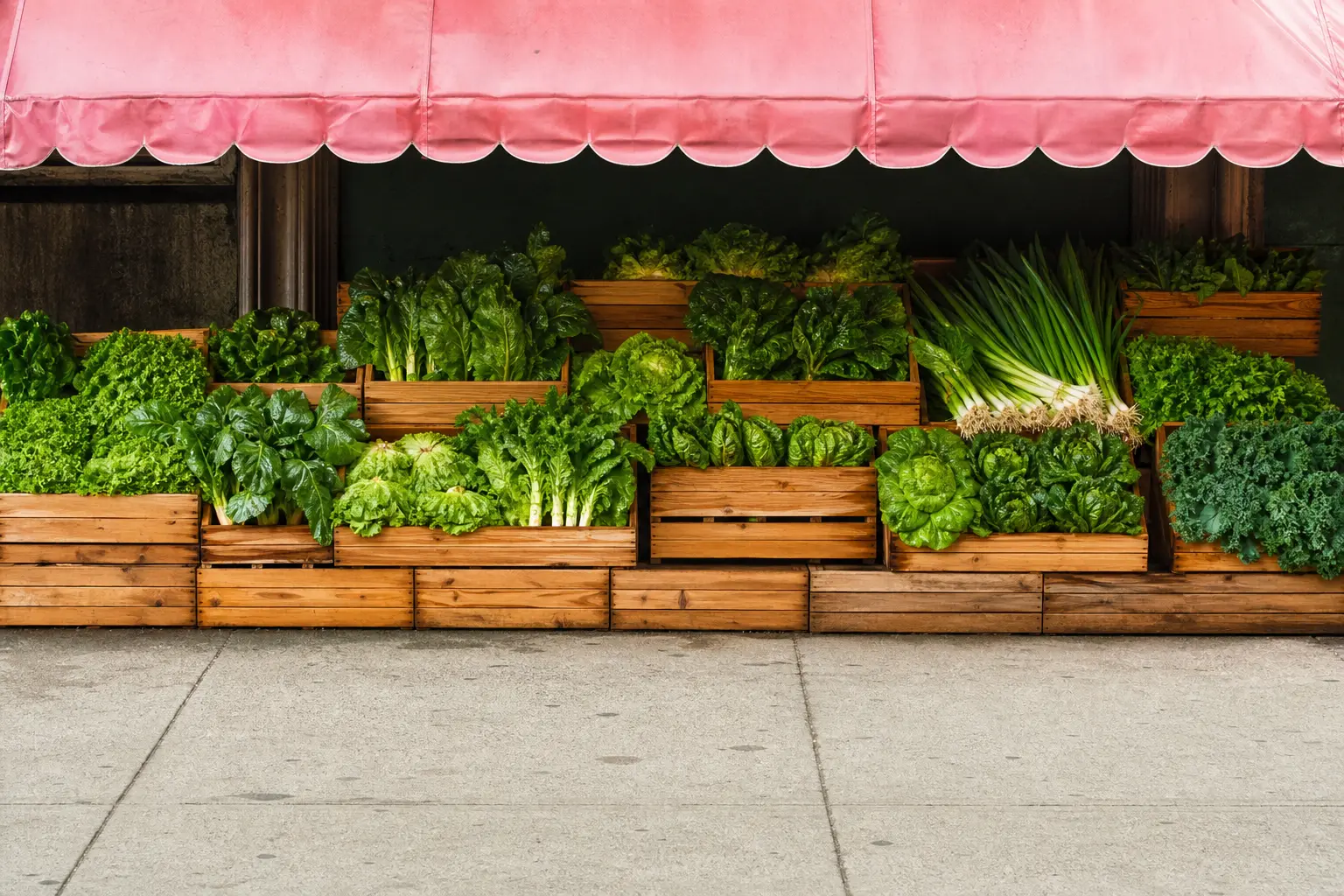 A market stall front with crates of green produce under a pink awning
