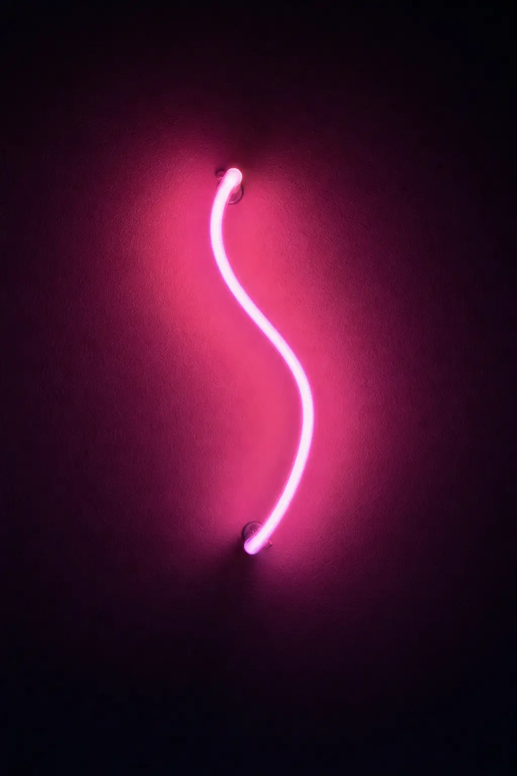 A blank neon tube glowing hot pink, curving against a dark wall